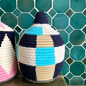 K&ouml;nnte beinhalten: Zwei gewebte K&ouml;rbe mit geometrischen Mustern. Der gr&ouml;&szlig;ere Korb ist blau, wei&szlig;, beige und t&uuml;rkis. Der kleinere Korb ist rosa, wei&szlig; und schwarz.