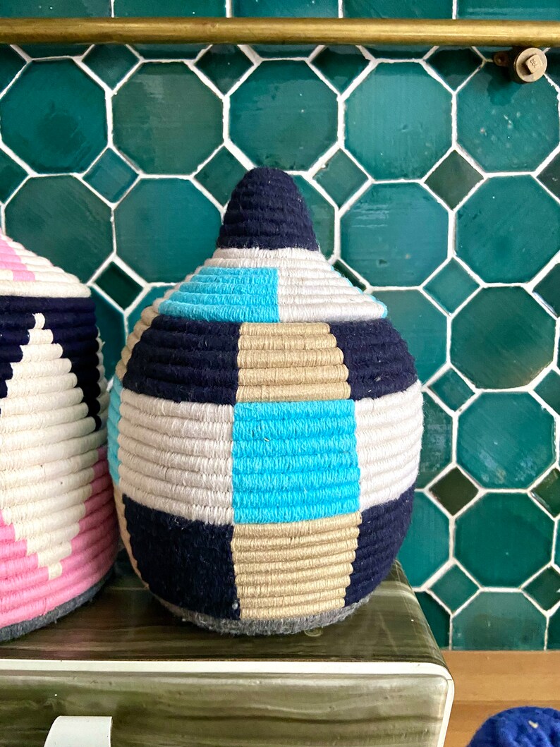 K&ouml;nnte beinhalten: Zwei gewebte K&ouml;rbe mit geometrischen Mustern. Der gr&ouml;&szlig;ere Korb ist blau, wei&szlig;, beige und t&uuml;rkis. Der kleinere Korb ist rosa, wei&szlig; und schwarz.