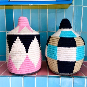 K&ouml;nnte beinhalten: Zwei gewebte Aufbewahrungsk&ouml;rbe mit geometrischen Mustern. Ein Korb ist pink, schwarz und wei&szlig;. Der andere Korb ist blau, schwarz, wei&szlig; und beige.