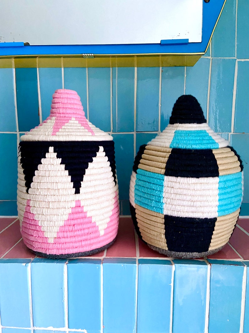 K&ouml;nnte beinhalten: Zwei gewebte Aufbewahrungsk&ouml;rbe mit geometrischen Mustern. Ein Korb ist pink, schwarz und wei&szlig;. Der andere Korb ist blau, schwarz, wei&szlig; und beige.