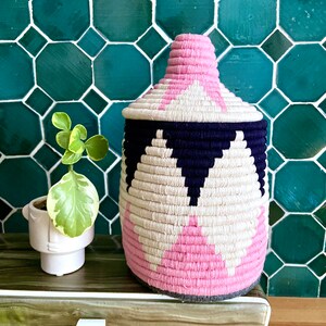 K&ouml;nnte beinhalten: Ein geflochtener Aufbewahrungskorb mit einem geometrischen Muster in Pink, Wei&szlig; und Schwarz. Der Korb steht auf einer Holzoberfl&auml;che.