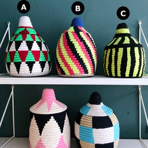 K&ouml;nnte beinhalten: F&uuml;nf gewebte Aufbewahrungsk&ouml;rbe mit verschiedenen geometrischen Mustern in Schwarz, Wei&szlig;, Rosa, Blau, Gr&uuml;n, Gelb und Beige. Die K&ouml;rbe sind auf zwei Regalen angeordnet.