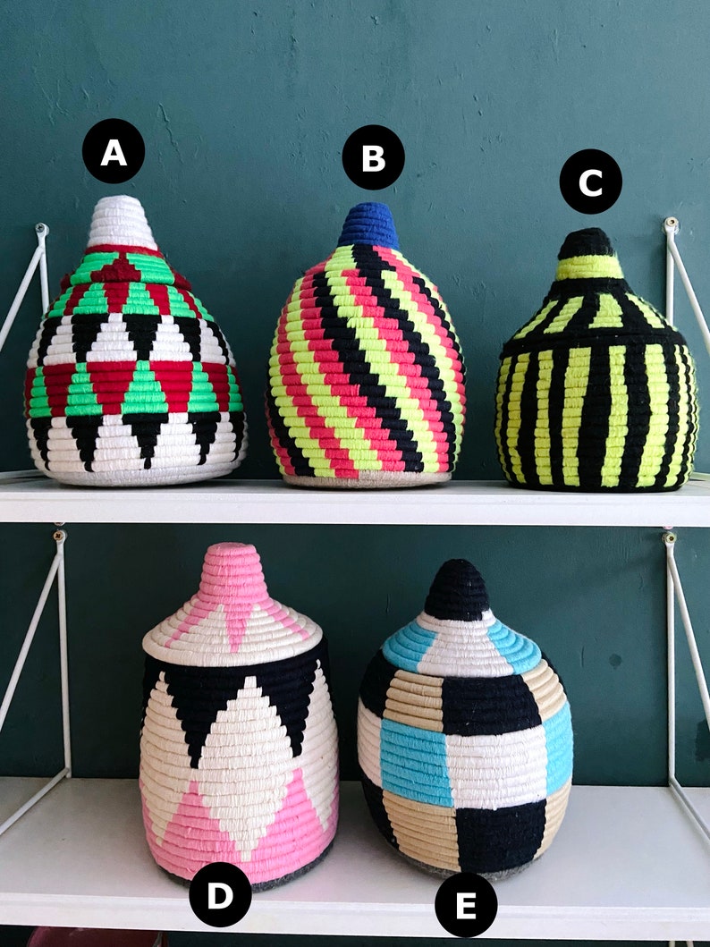 K&ouml;nnte beinhalten: F&uuml;nf gewebte Aufbewahrungsk&ouml;rbe mit verschiedenen geometrischen Mustern in Schwarz, Wei&szlig;, Rosa, Blau, Gr&uuml;n, Gelb und Beige. Die K&ouml;rbe sind auf zwei Regalen angeordnet.
