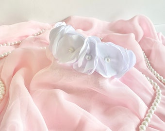 May include: A white flower headband with pearl accents on a pink fabric background.