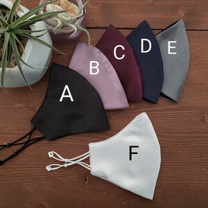 Op de afbeelding: Zes verschillende kleuren gezichtsmaskers, gelabeld van A tot en met F. De maskers zijn gemaakt van een gladde, zijdeachtige stof. De maskers hebben allemaal dezelfde vorm en grootte.