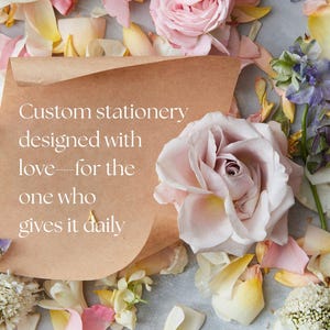 May include: A brown paper envelope with the text "Custom stationery designed with love - for the one who gives it daily" on it. The envelope is surrounded by pink and white rose petals.