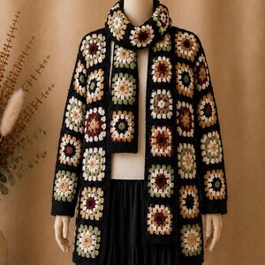 May include: A black crochet jacket and matching scarf set. The jacket and scarf are made of colorful granny squares in shades of cream, brown, green, and burgundy. The jacket is long-sleeved and open-fronted.