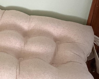 May include: A beige tufted cushion with a buttoned design. The cushion is made of a soft, textured fabric.