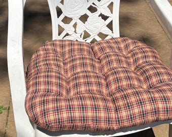 May include: A white plastic chair featuring a lattice backrest with embossed rose details. The chair includes a tufted seat cushion with a beige, red, and dark green plaid pattern, secured with visible stitching across the square tufted sections.