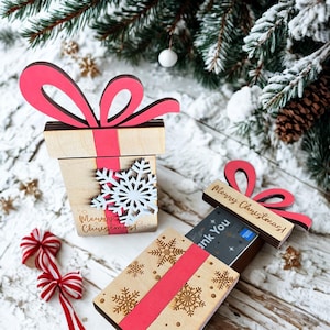 May include: Wooden gift box with a red bow and ribbon, decorated with snowflakes. The box has the text "Merry Christmas!" and is designed to hold cards. Festive holiday decor.
