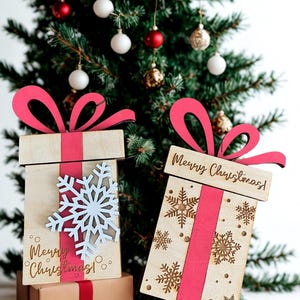 May include: Wooden Christmas gift boxes with red ribbon and bows, and snowflake and Merry Christmas! designs. The boxes are in front of a decorated Christmas tree with ornaments.
