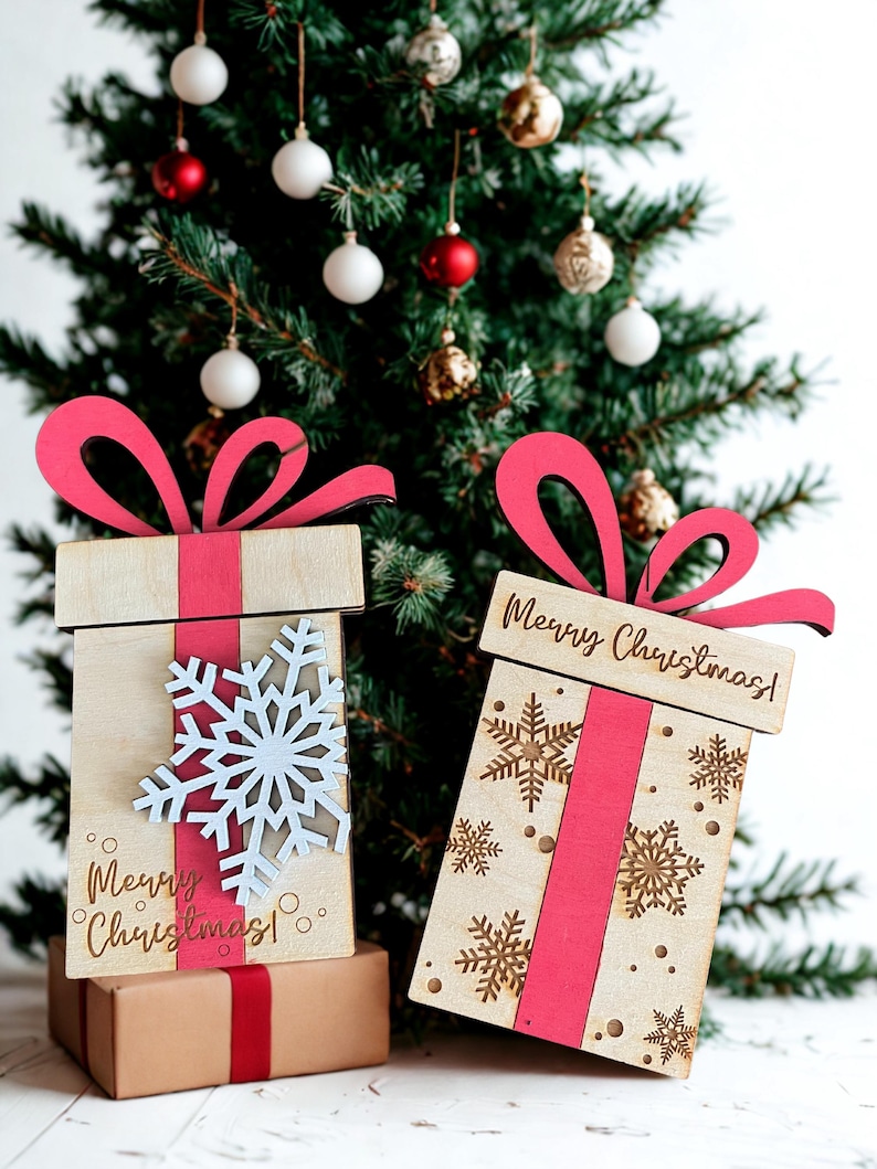 May include: Wooden Christmas gift boxes with red ribbon and bows, and snowflake and Merry Christmas! designs. The boxes are in front of a decorated Christmas tree with ornaments.