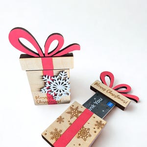 May include: Wooden gift box-shaped card holders with red ribbon accents and snowflake details. One box is open, revealing a card. The text "Merry Christmas!" is visible on the boxes.