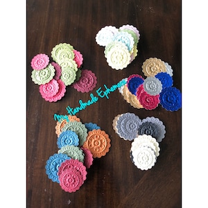 May include: A collection of colorful, die-cut paper ephemera in various shades, including pink, green, blue, and orange. Each piece has a scalloped edge and a floral design in the center. The text "My Handmade Ephemera" is visible.