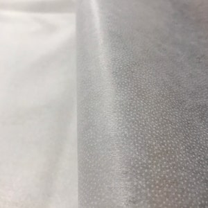 May include: White non-woven fabric with a textured surface. The fabric is folded in half, showing both sides.