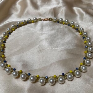 May include: A delicate necklace featuring large, round, white faux pearls. The pearls are strung on a gold-colored chain, interspersed with small yellow and blue beads. The necklace is secured with a copper-colored clasp.