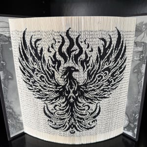 May include: A black and white book art sculpture of a phoenix rising from flames. The sculpture is made by folding the pages of a book to create a 3D design.