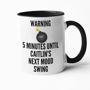 May include: White ceramic mug with a black interior and handle. The mug features the text "WARNING 5 MINUTES UNTIL CAITLIN'S NEXT MOOD SWING" in black, with a graphic of a black bomb with a yellow fuse.