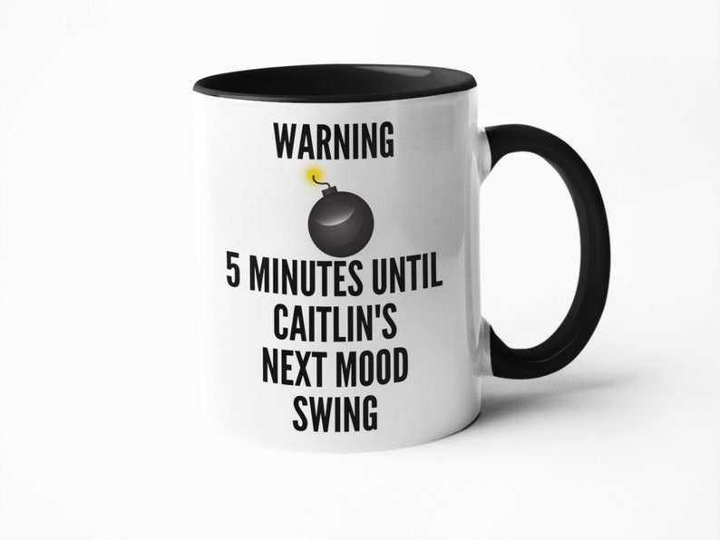 May include: White ceramic mug with a black interior and handle. The mug features the text "WARNING 5 MINUTES UNTIL CAITLIN'S NEXT MOOD SWING" in black, with a graphic of a black bomb with a yellow fuse.