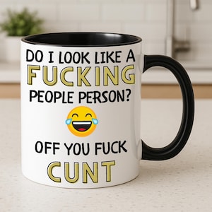 May include: A white ceramic mug with a black interior and handle. The front features black text that reads: DO I LOOK LIKE A FUCKING PEOPLE PERSON? followed by a laughing emoji with tears, and the text: OFF YOU FUCK CUNT in bold black letters.