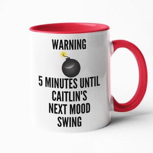 May include: White ceramic mug with a red interior and handle. The mug features the text "WARNING 5 MINUTES UNTIL CAITLIN'S NEXT MOOD SWING" with a cartoon bomb graphic. A humorous gift idea.