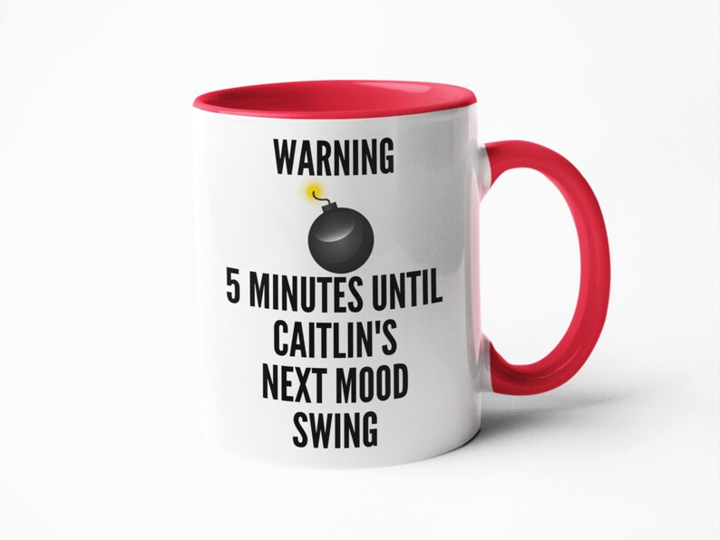 May include: White ceramic mug with a red interior and handle. The mug features the text "WARNING 5 MINUTES UNTIL CAITLIN'S NEXT MOOD SWING" with a cartoon bomb graphic. A humorous gift idea.
