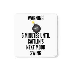 May include: A white square coaster with black text and a cartoon bomb graphic. The text reads "WARNING 5 MINUTES UNTIL CAITLIN'S NEXT MOOD SWING."