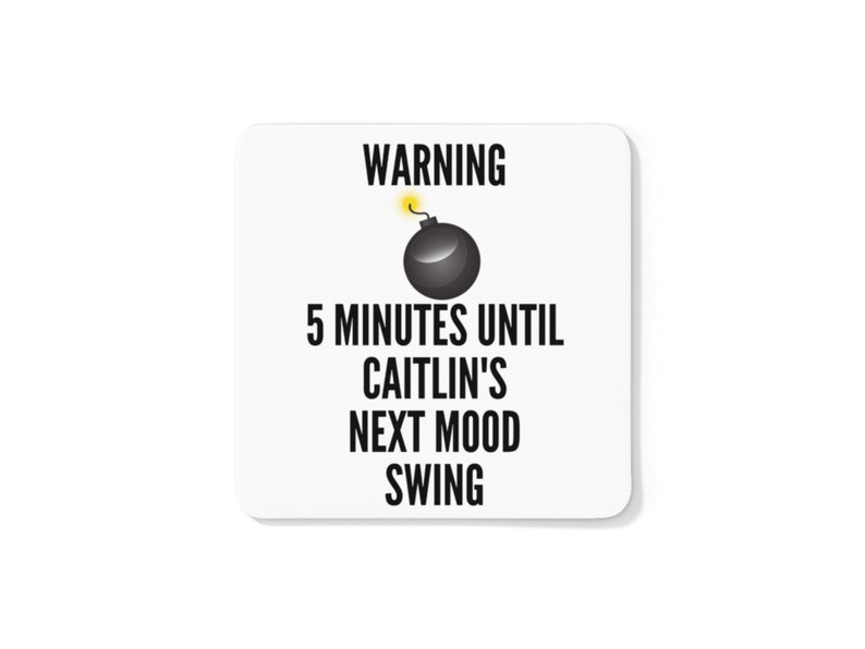 May include: A white square coaster with black text and a cartoon bomb graphic. The text reads "WARNING 5 MINUTES UNTIL CAITLIN'S NEXT MOOD SWING."