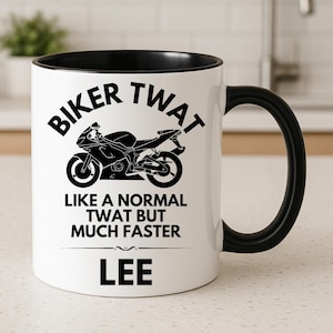 May include: A white ceramic mug with a black interior and handle. The front features a black graphic of a motorcycle and the text: BIKER TWAT LIKE A NORMAL TWAT BUT MUCH FASTER LEE. The design is printed in a bold, black, sans-serif font.