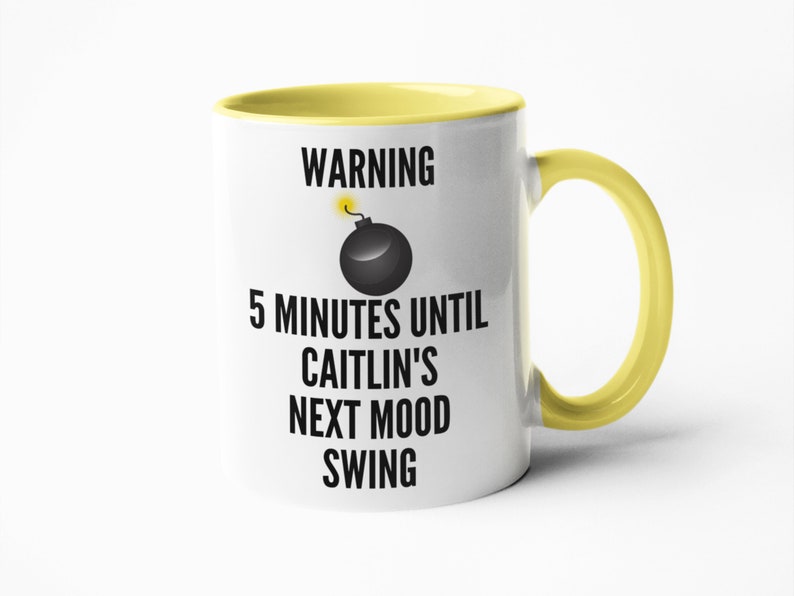 May include: White ceramic mug with a yellow interior and handle. The mug features the text "WARNING 5 MINUTES UNTIL CAITLIN'S NEXT MOOD SWING" with a cartoon bomb graphic. The mug is designed for beverages.