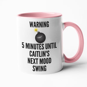 May include: White ceramic mug with a pink interior and handle. The mug features the text "WARNING 5 MINUTES UNTIL CAITLIN'S NEXT MOOD SWING" with a black bomb graphic and yellow fuse.