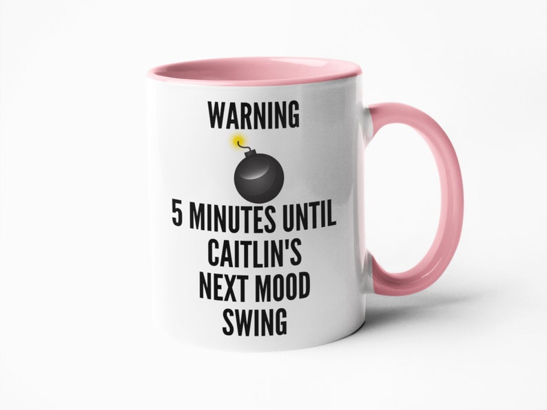 May include: White ceramic mug with a pink interior and handle. The mug features the text "WARNING 5 MINUTES UNTIL CAITLIN'S NEXT MOOD SWING" with a black bomb graphic and yellow fuse.