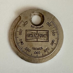 May include: A silver Champion spark plug gap opener tool. The tool has a circular shape with measurements in inches from .020 to .100. The word "Champion" is printed in a rectangular box in the center.