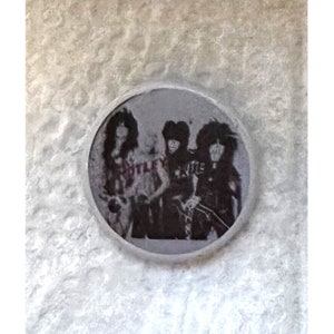 May include: A black and white photo of a band, possibly Kiss, in a circular frame. The band members are wearing black clothing and have long hair. The word "KISS" is visible on the photo.