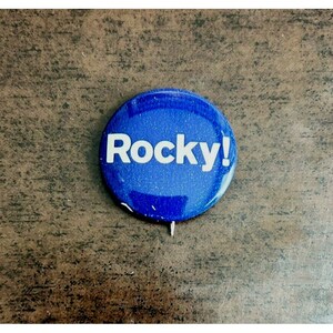 May include: A blue button with white lettering that reads "Rocky!"