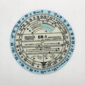 May include: A blue and white circular flight computer with the text "ER-1 PROFESSIONAL FLIGHT COMPUTER" and "INSTITUTE FOR AERONAUTICAL EDUCATION" printed on it. The computer has a variety of scales and markings for calculating airspeed, altitude, and other flight parameters.