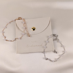 K&ouml;nnte beinhalten: Zwei Perlenarmb&auml;nder in einem wei&szlig;en Samtbeutel mit dem Text "To My Bridesmaid".