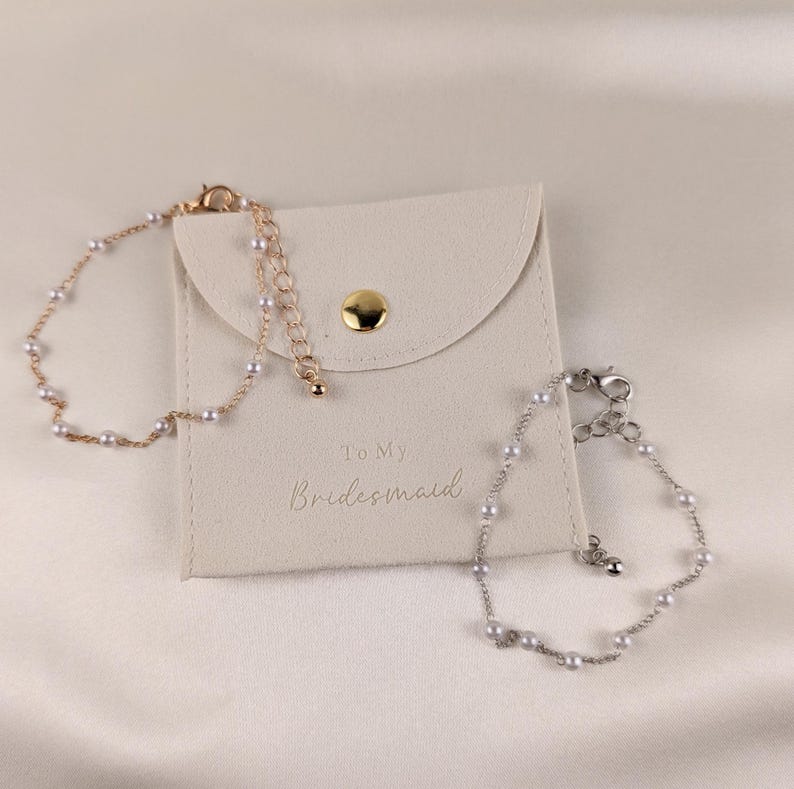 K&ouml;nnte beinhalten: Zwei Perlenarmb&auml;nder in einem wei&szlig;en Samtbeutel mit dem Text "To My Bridesmaid".