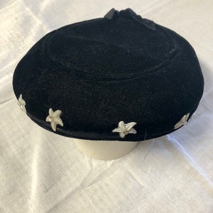 May include: A black velvet hat with white star-shaped embellishments around the brim.