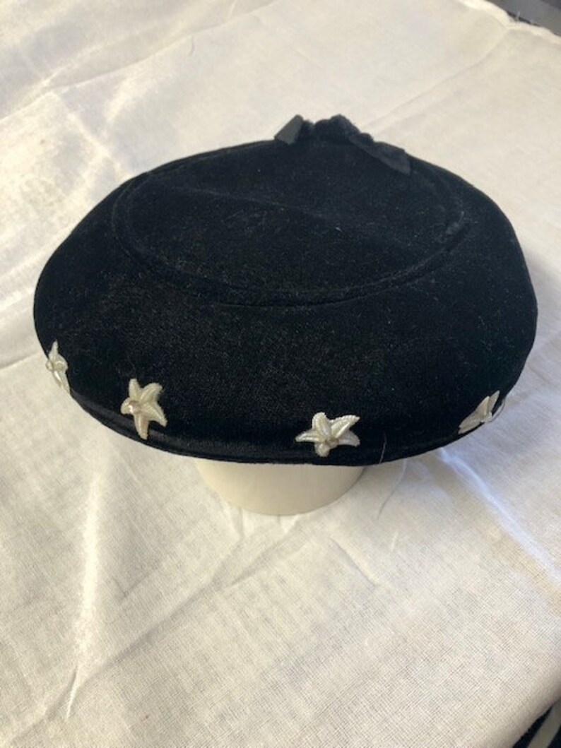 May include: A black velvet hat with white star-shaped embellishments around the brim.