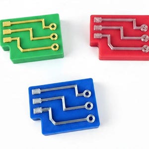 May include: Three rectangular blocks in green, red, and blue, each featuring a raised circuit board pattern on the surface. The green block has gold-colored traces, the red block has translucent traces, and the blue block has silver-colored traces.