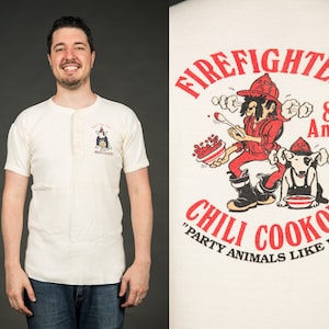May include: White t-shirt with a red, white and blue illustration of a dog wearing a chef's hat and holding a bowl of chili. The text "Firefighters 8th Annual Chili Cookoff "Party Animals Like It Hot" is printed on the shirt.
