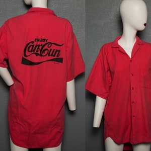 Può includere: Camicia rossa a maniche corte con bottoni e una stampa nera sul retro che dice "Enjoy Can-Cun".