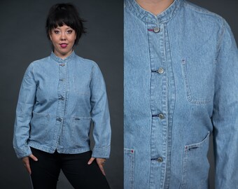 May include: A light blue denim jacket with a mandarin collar and button closure. The jacket has two pockets on the front and a striped pattern.