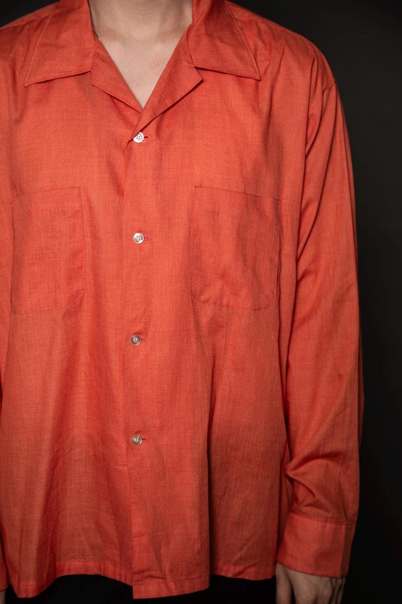 Puede incluir: Una camisa de manga larga de color naranja con botones, cuello y dos bolsillos en el pecho.