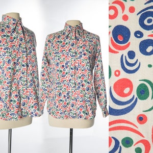Peut inclure: Une chemise blanche à manches longues boutonnée avec un motif abstrait coloré de cercles et de volutes rouges, bleus, verts et blancs.