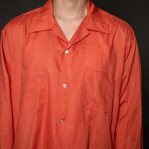 Puede incluir: Una camisa de manga larga de color naranja con botones, cuello y dos bolsillos.