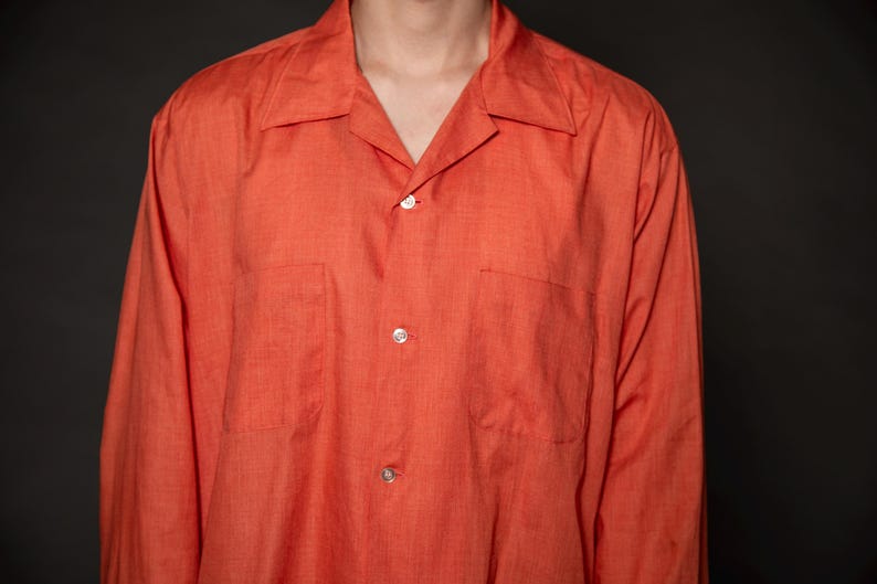 Puede incluir: Una camisa de manga larga de color naranja con botones, cuello y dos bolsillos.