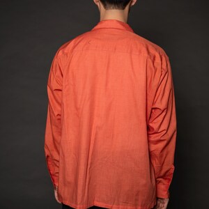 Puede incluir: Una camisa de manga larga de color coral con cuello abotonado. La camisa est&aacute; hecha de una tela ligera y tiene un corte holgado.