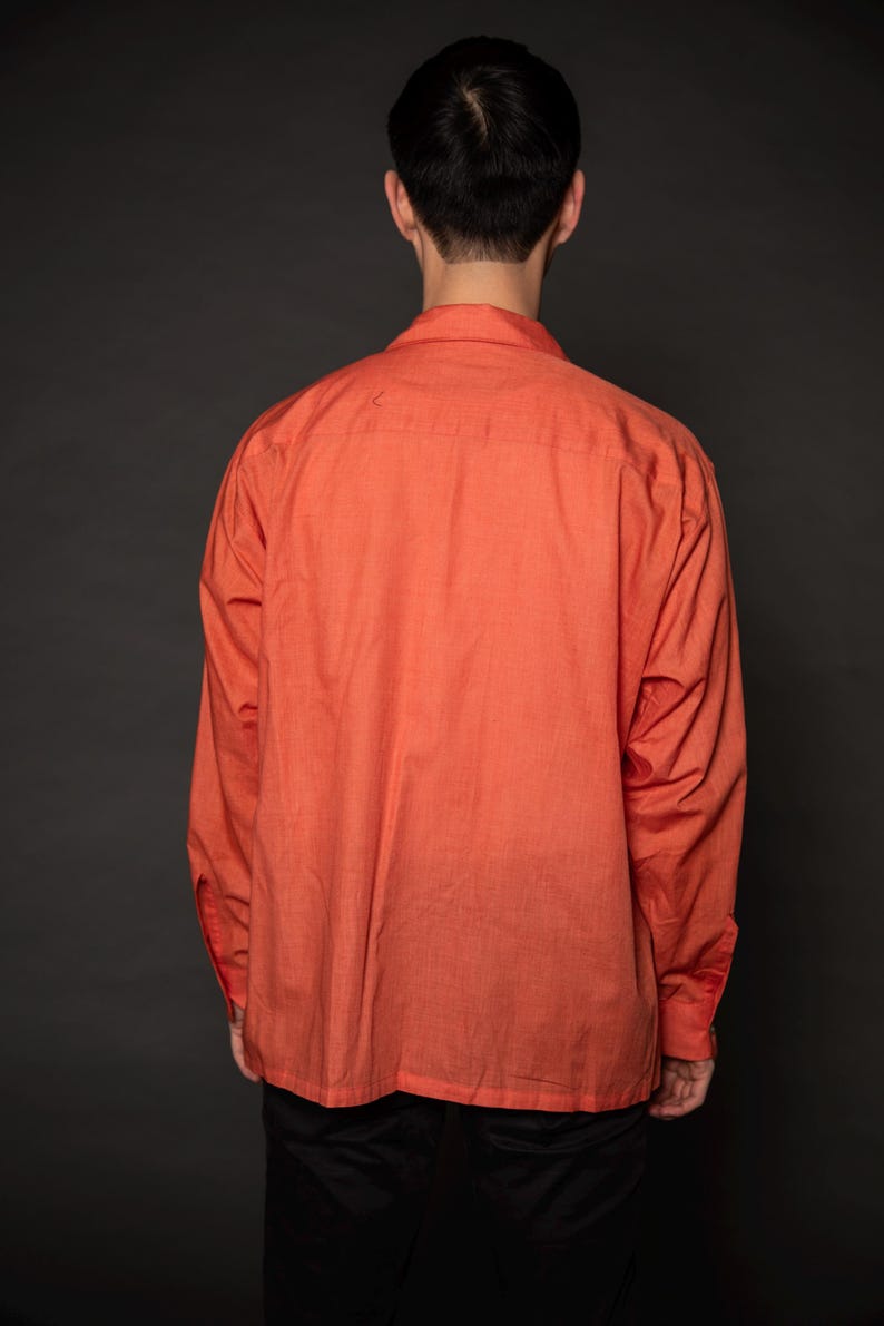 Puede incluir: Una camisa de manga larga de color coral con cuello abotonado. La camisa est&aacute; hecha de una tela ligera y tiene un corte holgado.